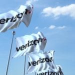 Waving flags with Verizon logo against sky, editorial 3D rendering